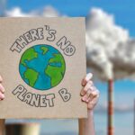 sinnbildlich für die Western Climate Initiative Schild mit der Aufschrift "There's no Planet B" vor dem Hintergrund rauchender Schlote